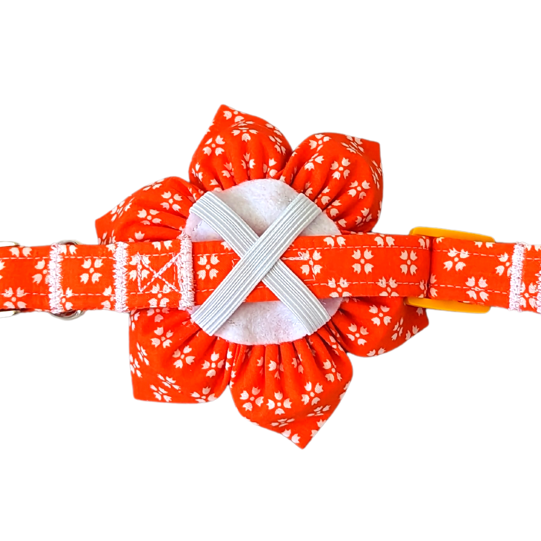 Image showing the back of the Bright Orange with Whimsical White Floral Kanzashi Flower with a collar looped through the elastic X shape. The flower has a round felt backing with stitched garters.